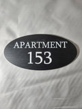 Custom oval black apartment number sign with white text reading 'Apartment 153'
