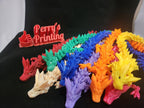 Colorful 3D printed dragon models and Perry's Printing sign on black background.