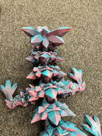 3D printed articulated dragon in pink and blue filament on textured carpet