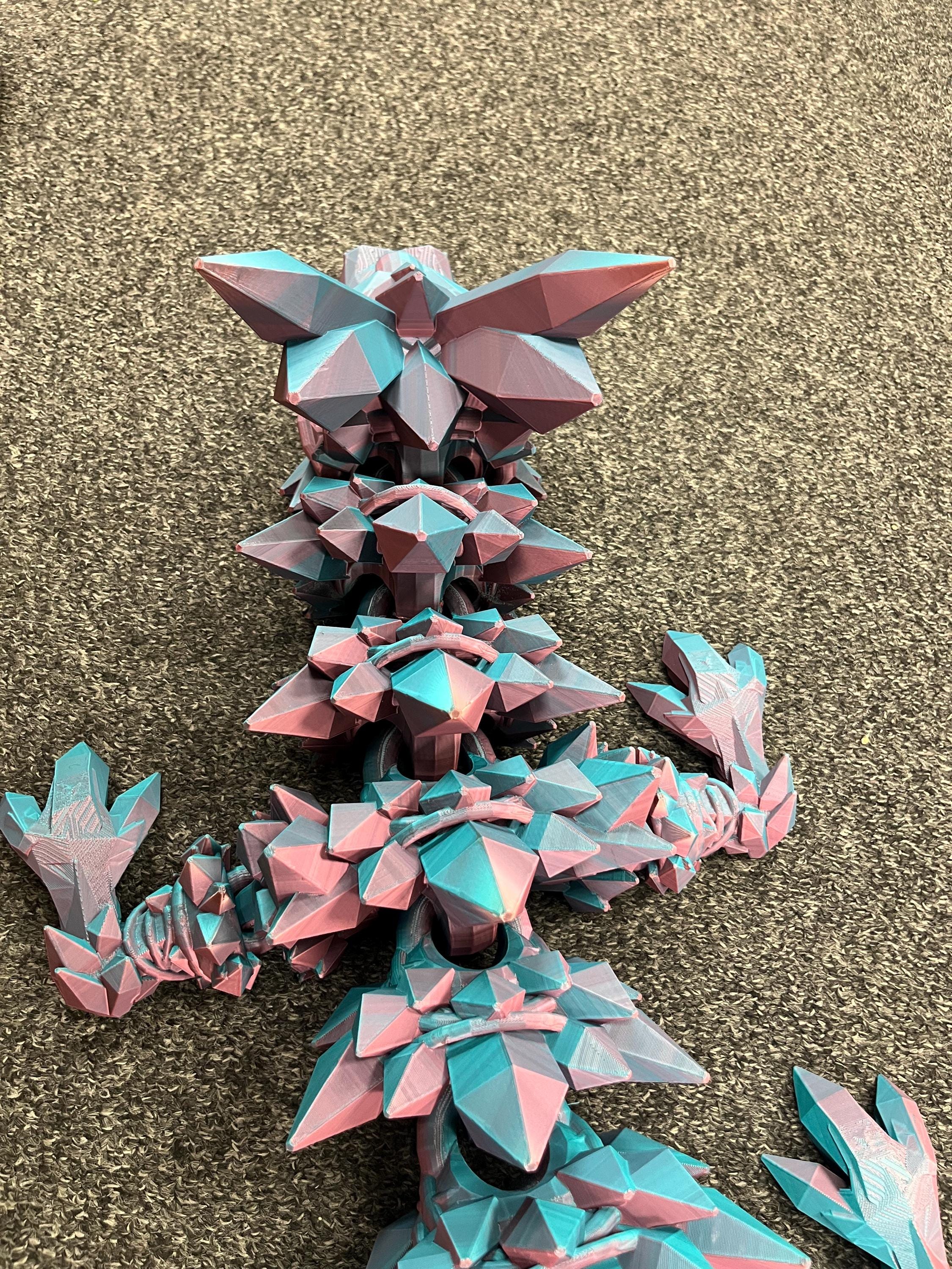 3D printed articulated dragon in pink and blue filament on textured carpet