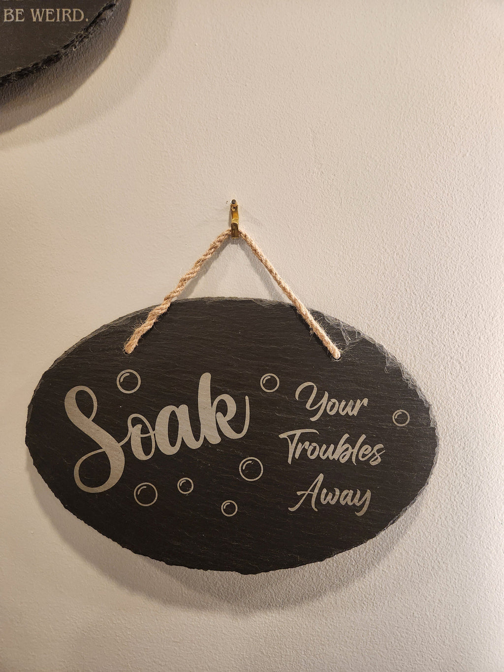Laser engraved slate bathroom sign with 'Soak Your Troubles Away' text and bubbles, hanging on wall.