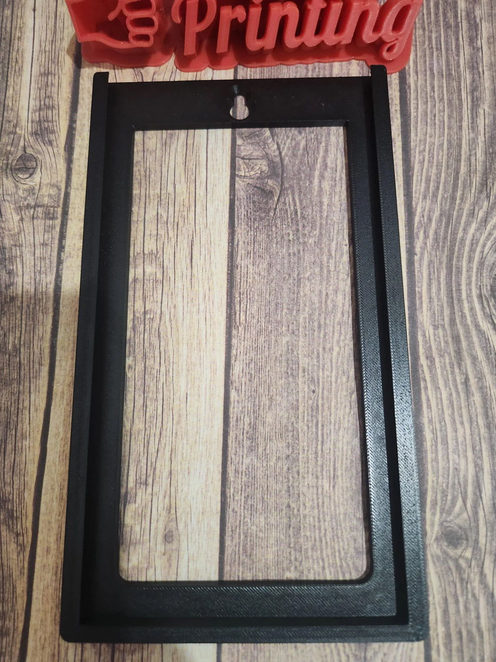 3D printed black rectangular frame with mounting hole on wood surface