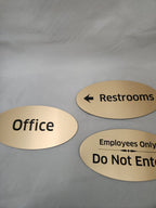 Three gold oval office signs for restrooms, employees only, and office on a white background.