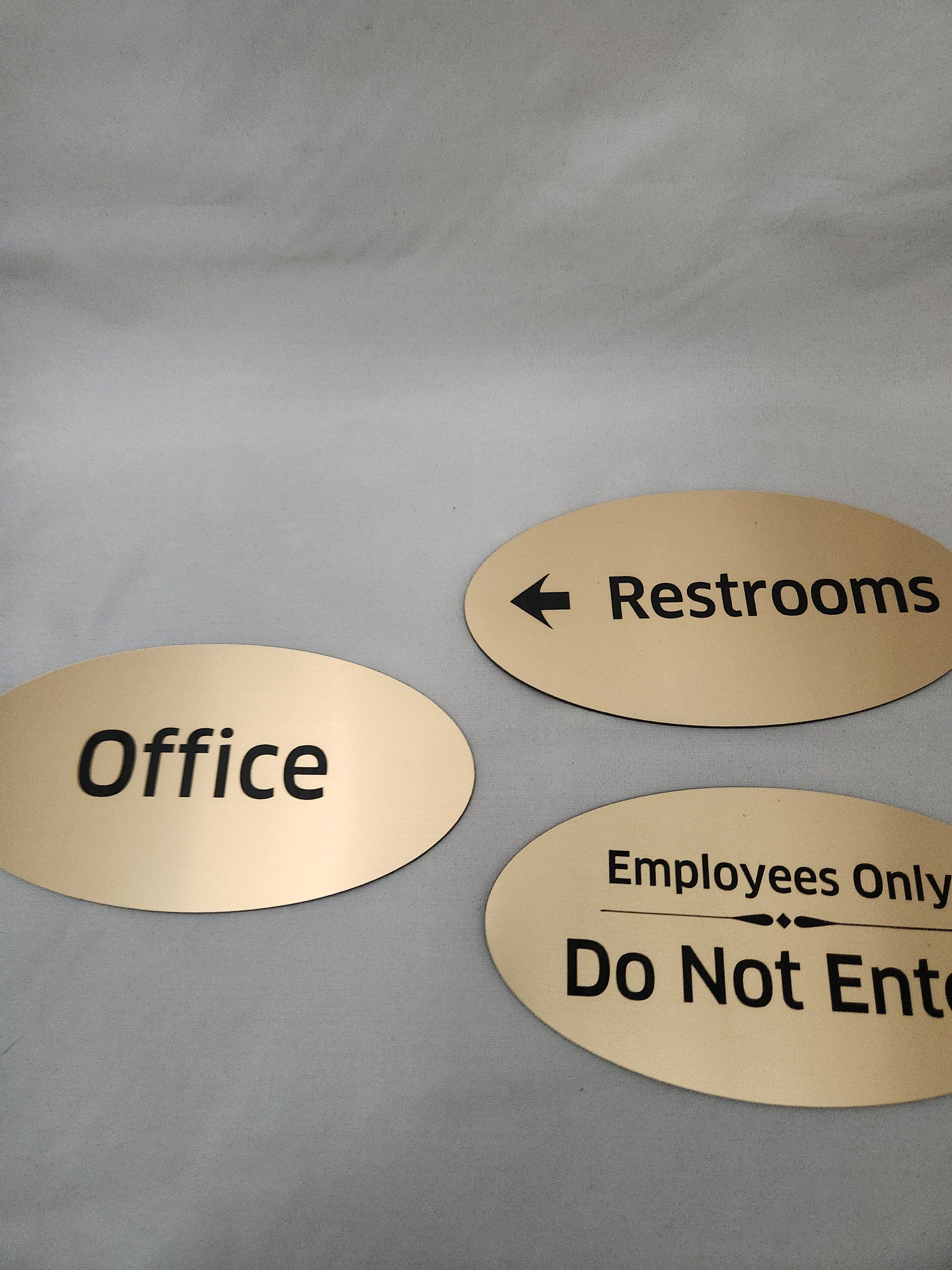 Three gold oval office signs for restrooms, employees only, and office on a white background.