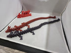 Two articulated 3D printed dragon figurines, one red and one black, on a display surface.