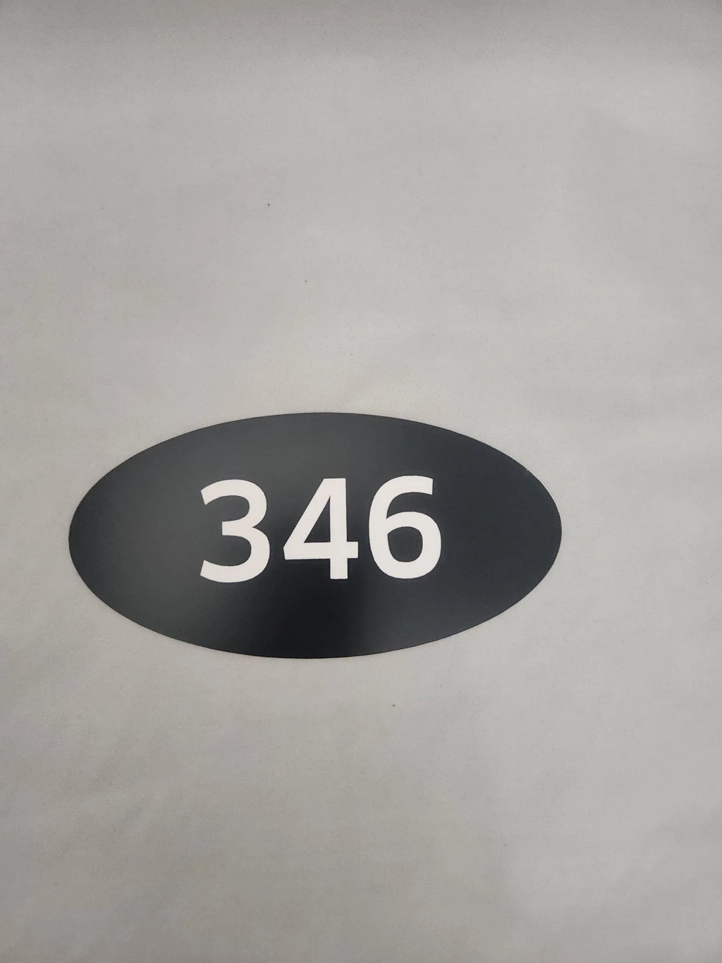 Oval black custom number sign with white 346 on a neutral background