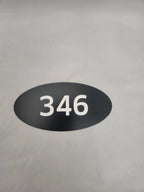 Oval black custom number sign with white 346 on a neutral background