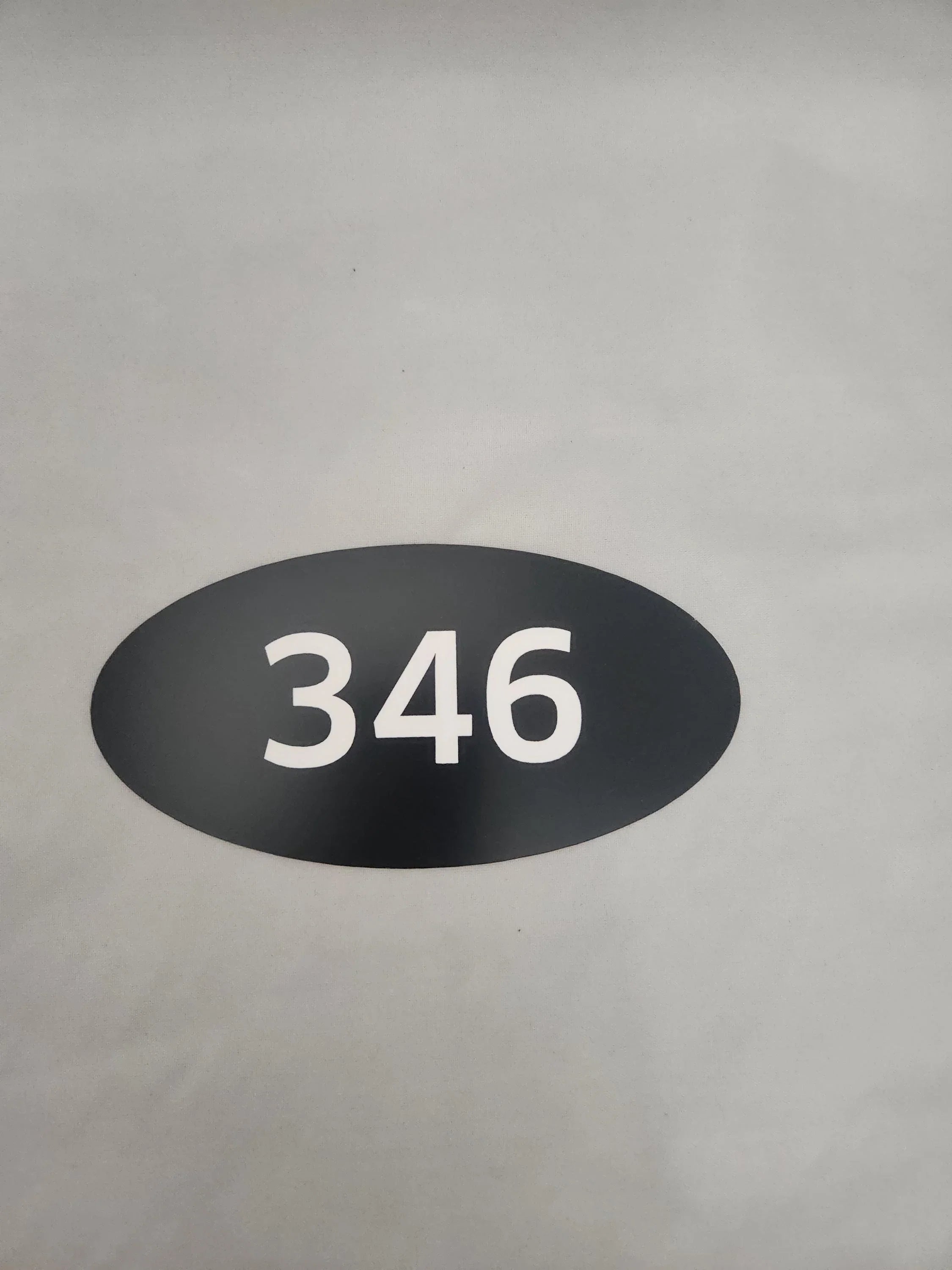 Oval black custom number sign with white 346 on a neutral background