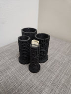 3D printed black puzzle tubes with geometric patterns, one holding rolled cash, on a table