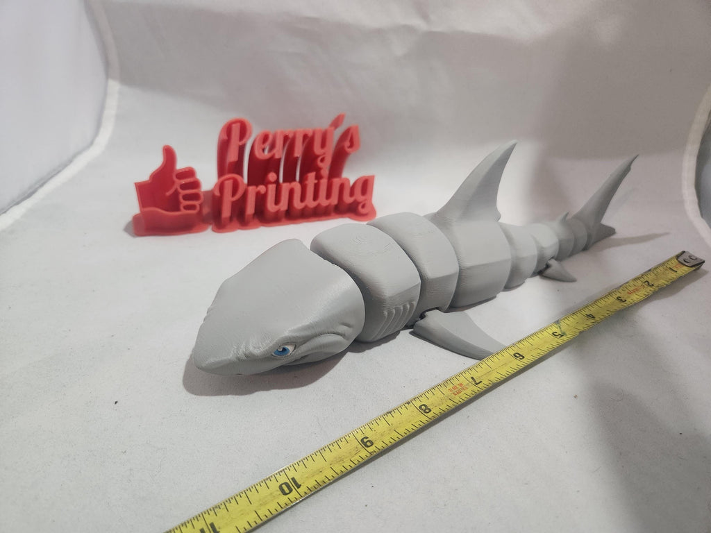 3D printed articulated shark figurine beside measuring tape and red thumbs up sign