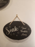 Laser engraved slate sign with 'Soak your troubles away' hanging on a wall, decorative bathroom decor.