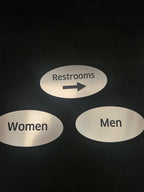 Brushed metal restroom signs for men and women with an arrow directional sign
