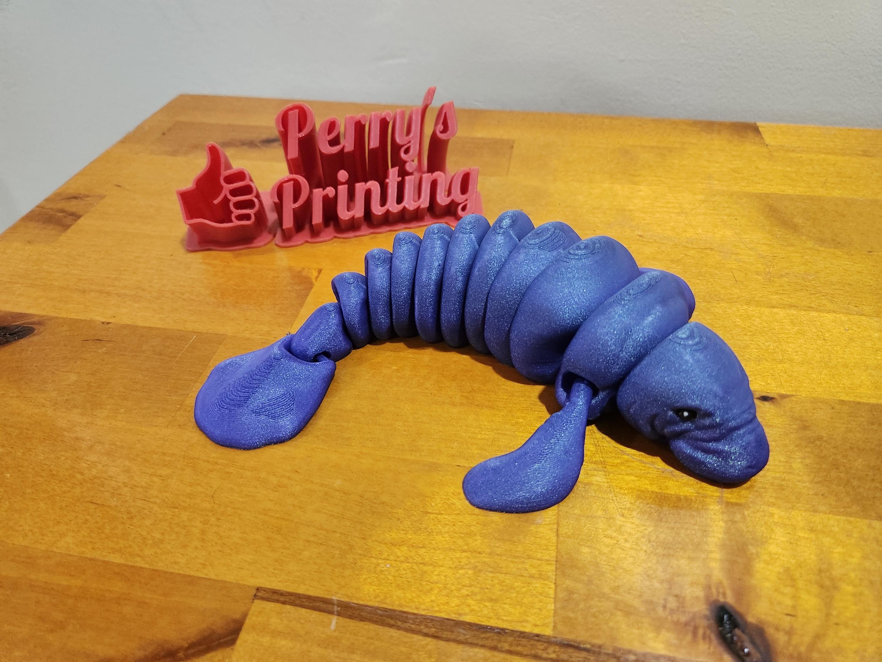 3D printed articulated blue manatee figurine on wood table with Perry's Printing sign