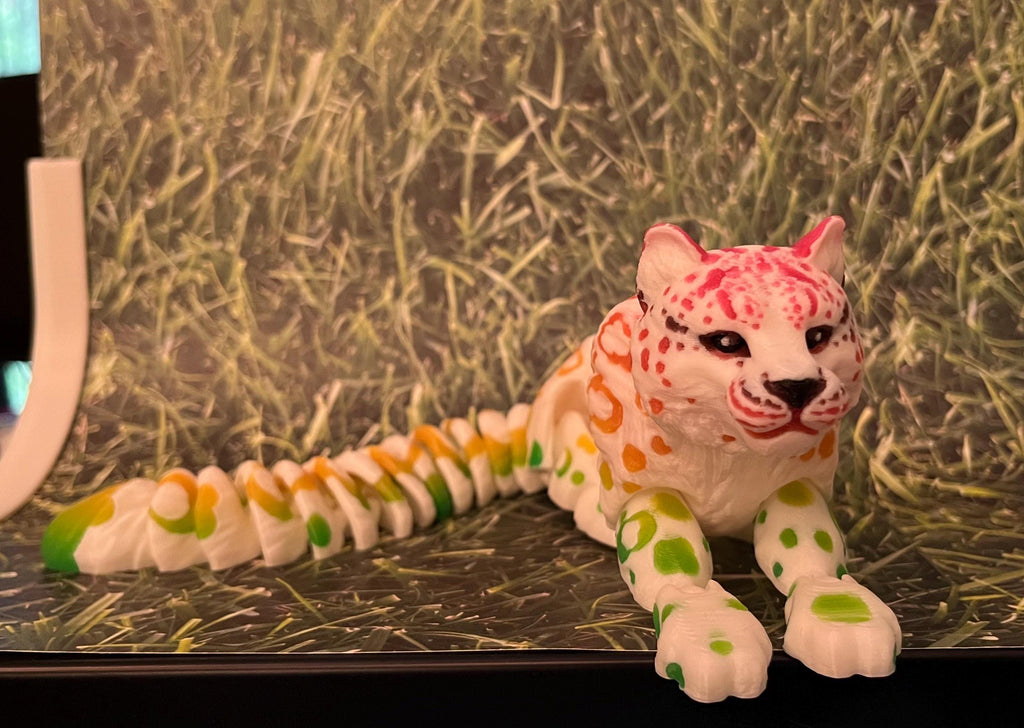 Colorful 3D printed articulated leopard figurine with green, yellow, and pink spots on grass