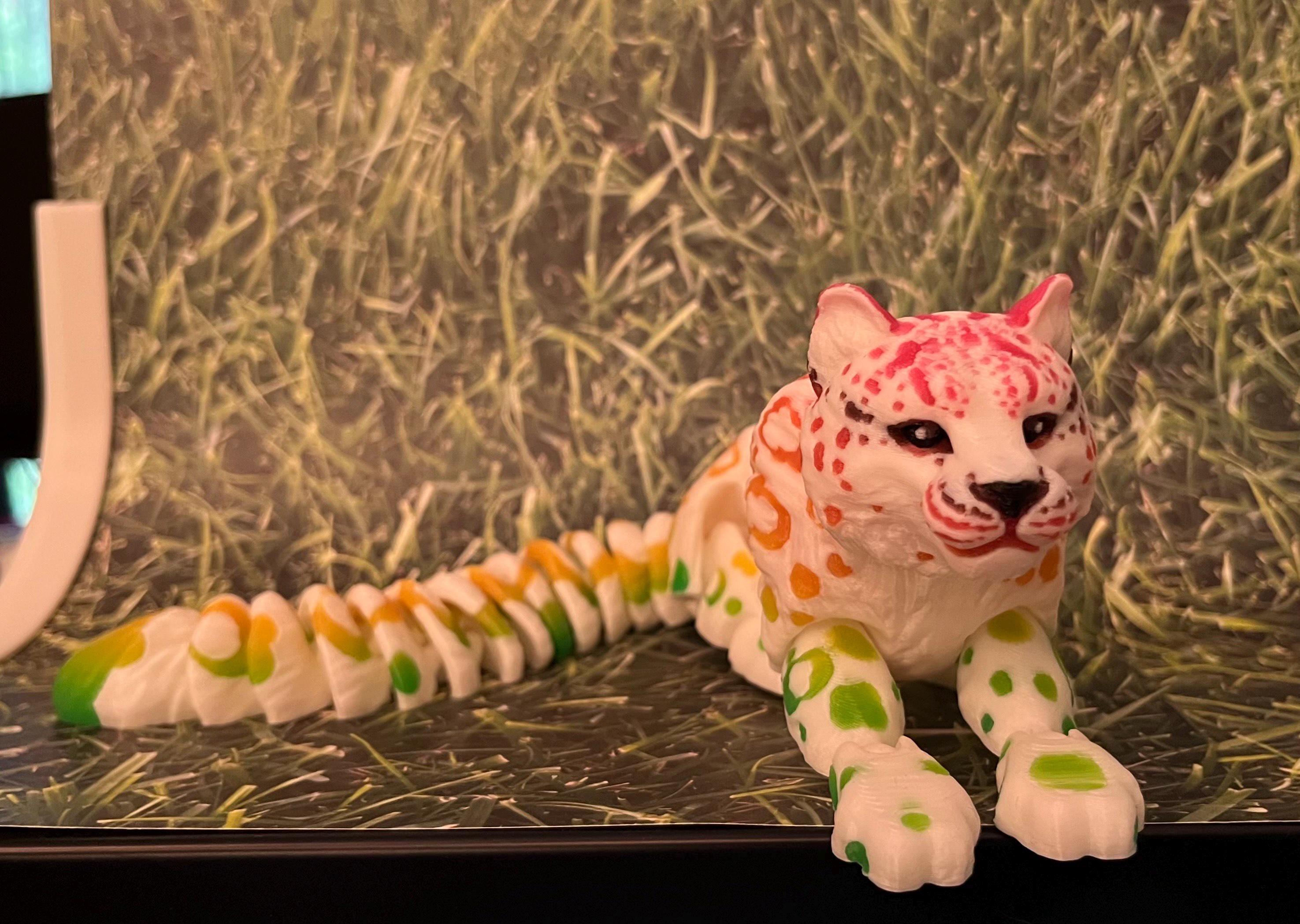 Colorful 3D printed articulated leopard figurine with green, yellow, and pink spots on grass
