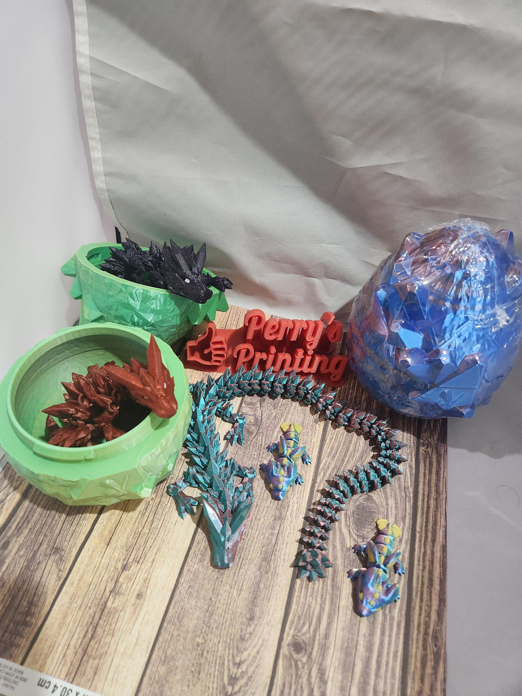 Colorful 3D printed dragons, lizard figures, and a red 'Printing' sign on wood surface.