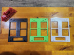 Three 3D printed multi-gang switch plates in black, green, and white on a wooden surface