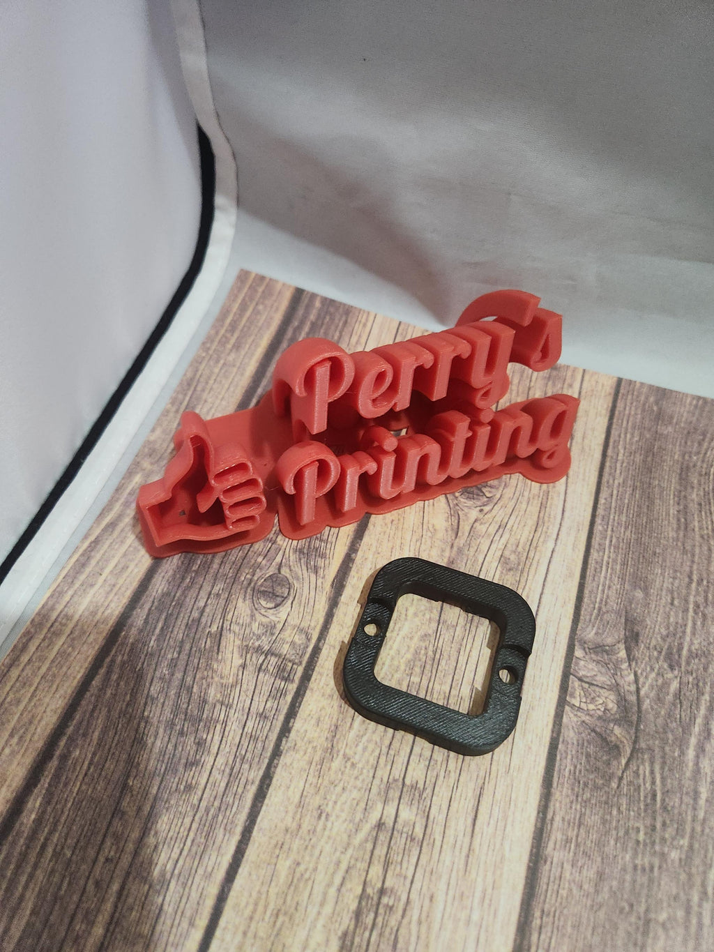 3D printed red Perry's Printing sign with thumb up and black plastic mounting bracket on wood table
