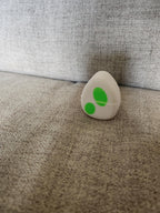 3D printed white egg with green spots on a light gray fabric background