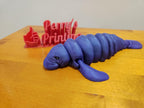 3D printed purple manatee figurine on wood table with red engraved sign in background