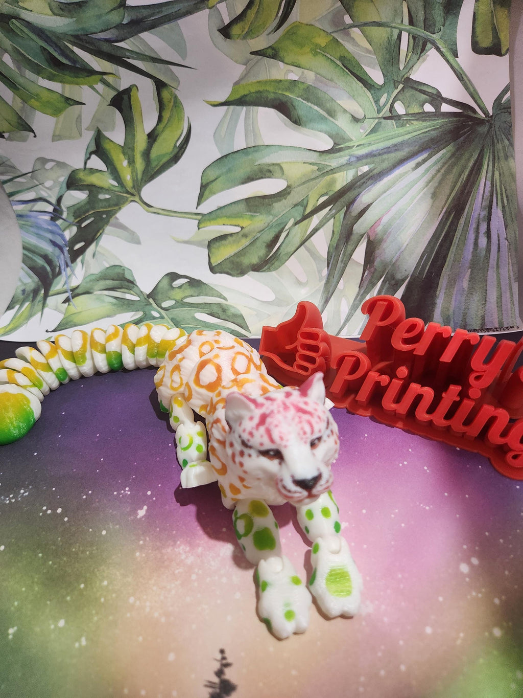 Colorful 3D printed leopard figure on gradient surface with leafy background and red 'Printing' sign