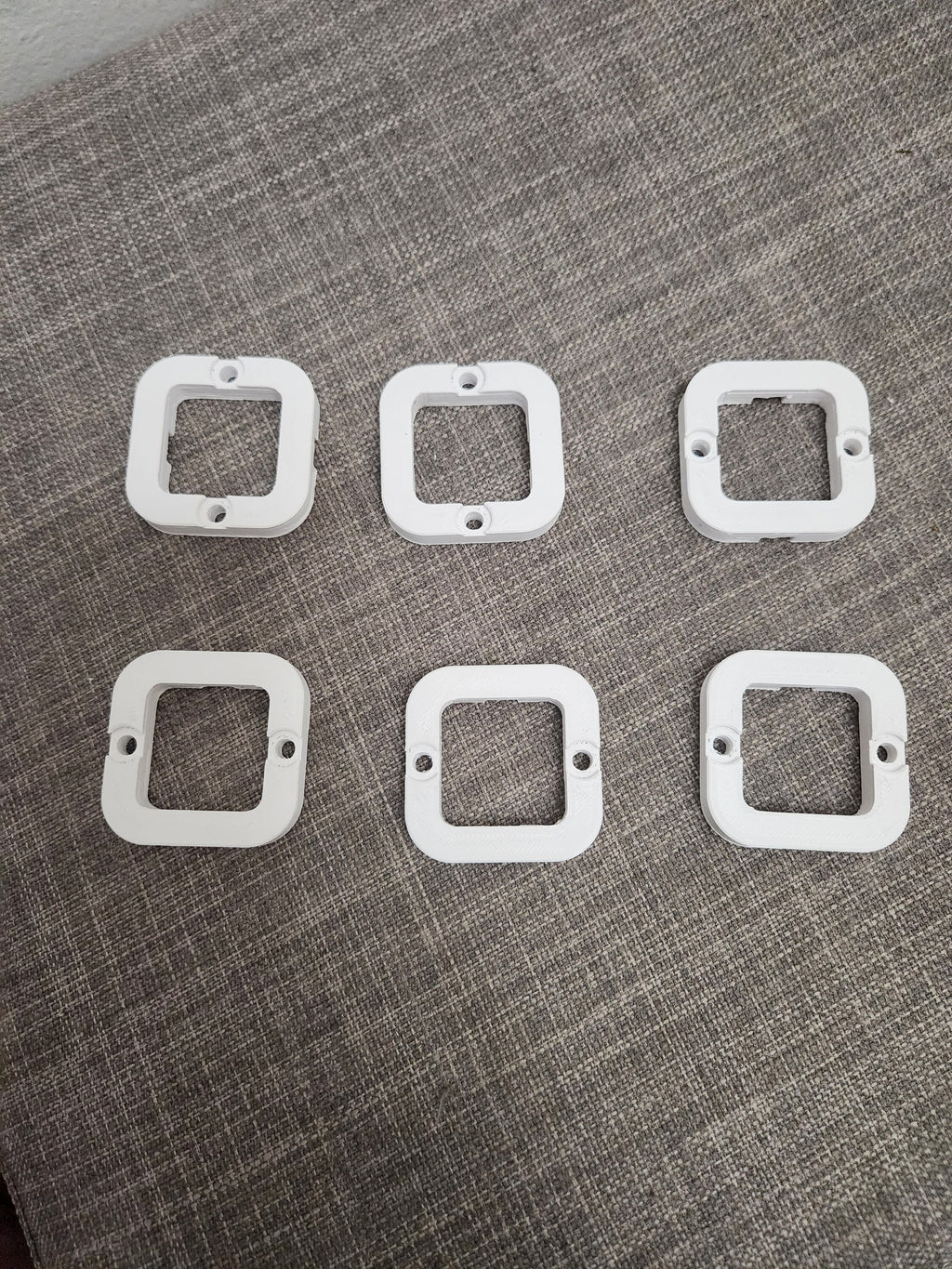 Set of six white 3D printed plastic square mounting brackets on textured gray fabric