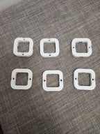 Set of six white 3D printed plastic square mounting brackets on textured gray fabric