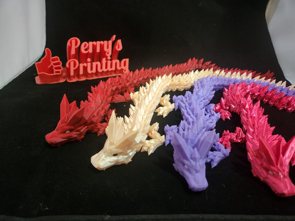 3D printed articulated dragon figures in red, cream, purple, and pink on black fabric
