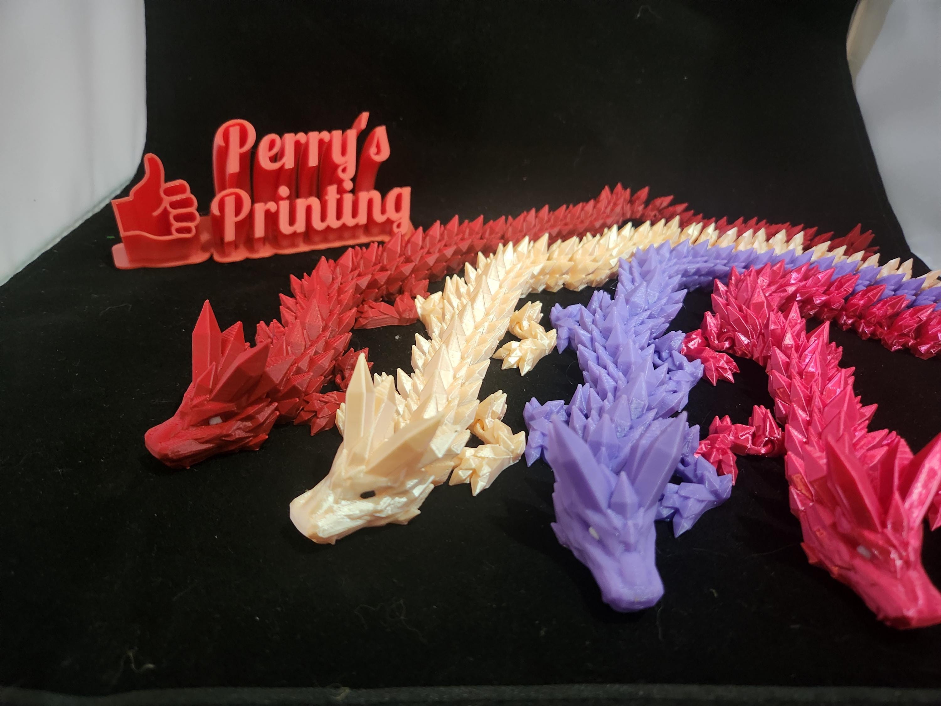 3D printed articulated dragon figures in red, cream, purple, and pink on black fabric