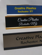 Custom engraved plastic desk name plates in blue, black, and gold with bold text