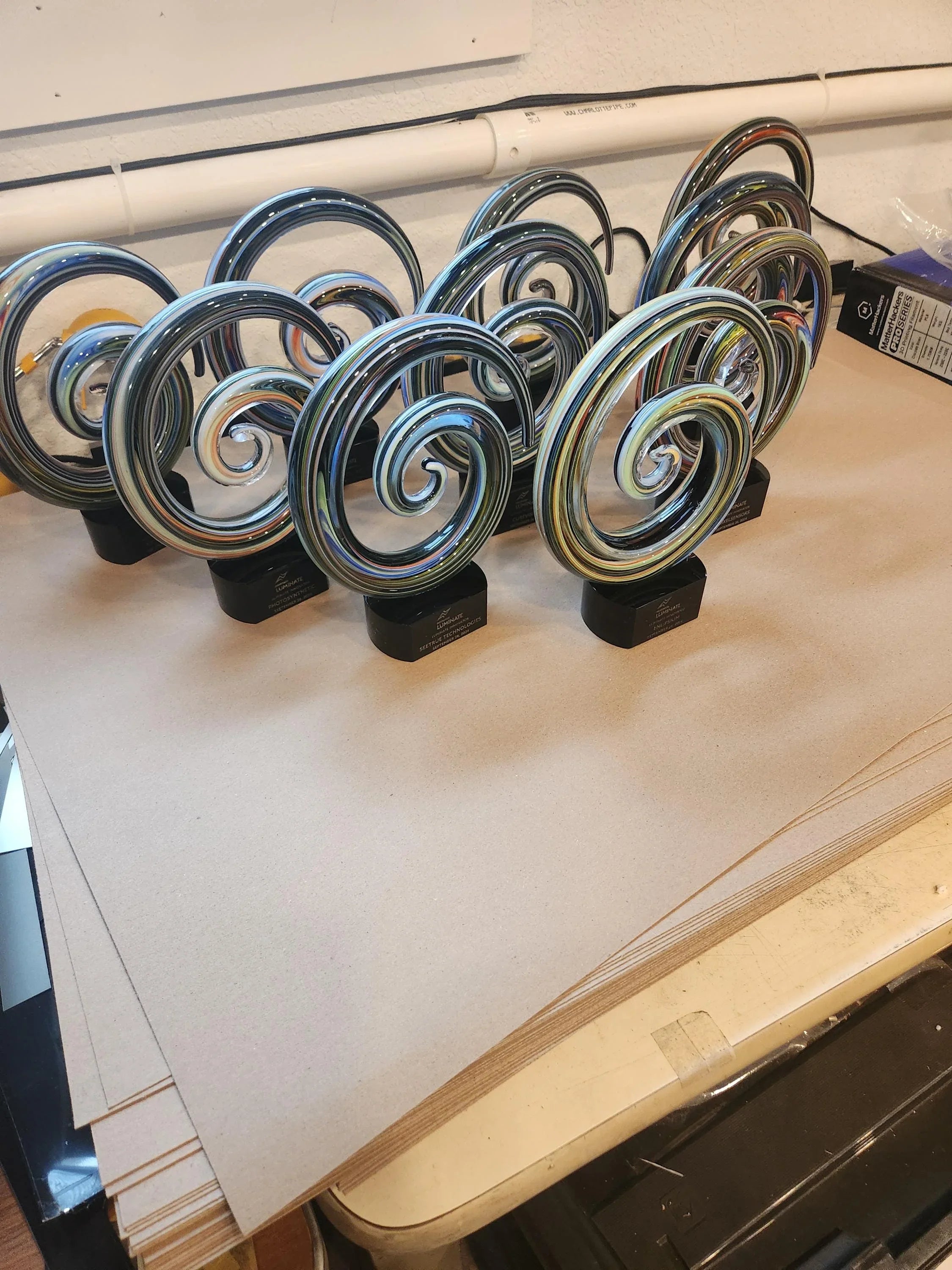 Multiple glass spiral awards with black bases displayed on a table, custom engraved trophies
