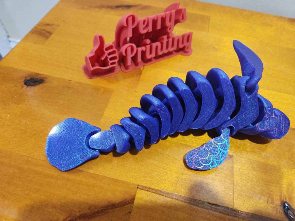 Blue 3D printed articulated sea creature toy on wood, red custom sign in background