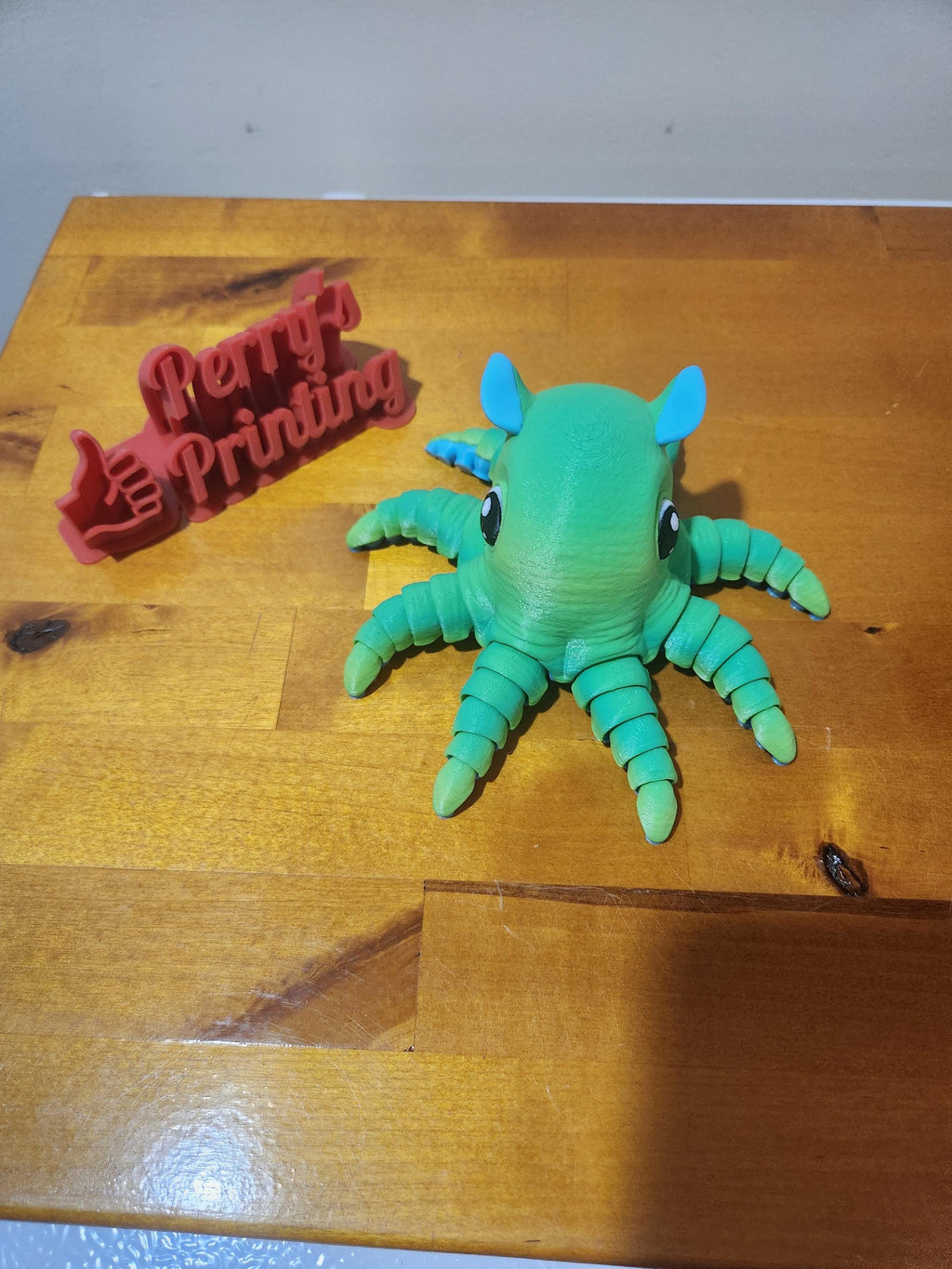 3D printed green octopus figurine and red Perry's Printing sign on wooden surface