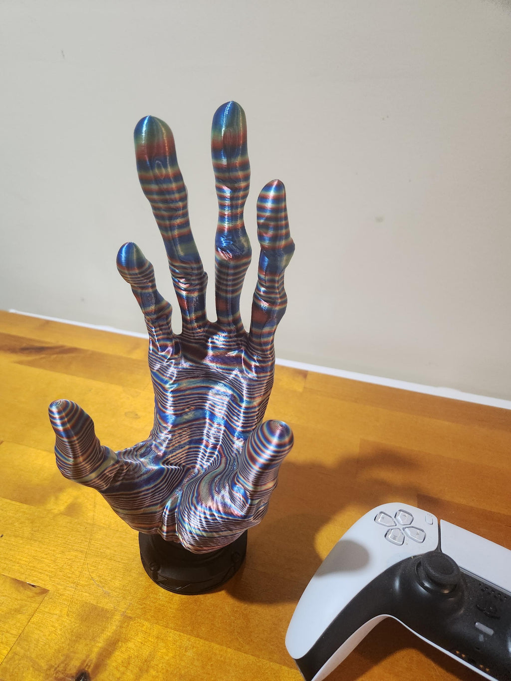 Colorful 3D printed hand sculpture with striped pattern next to a gaming controller on wood surface
