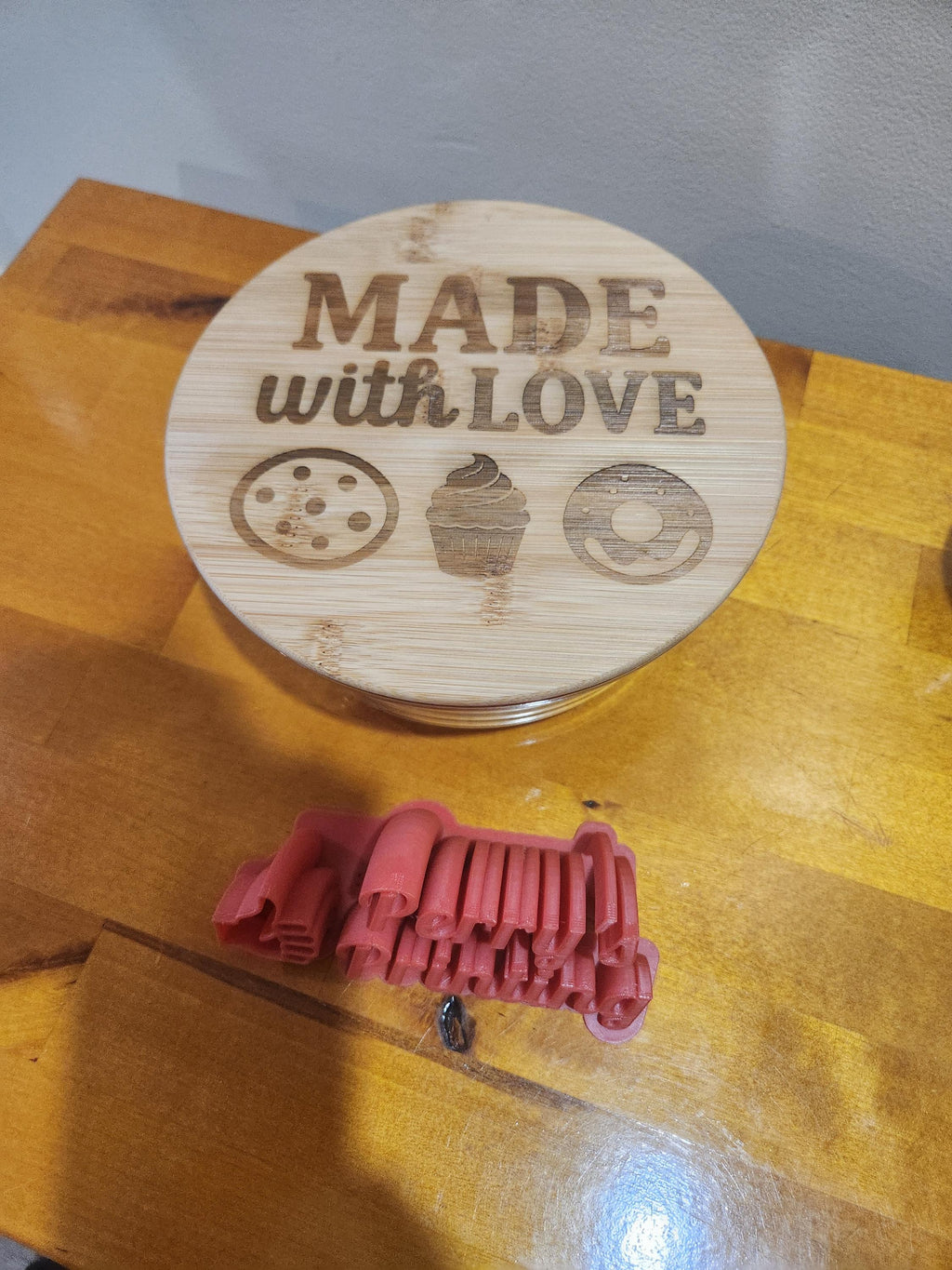 Wooden lid laser engraved with 'Made with Love' and pastry icons, red 3D-printed object nearby