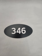 Black oval adhesive sign with white number 346 on a plain background