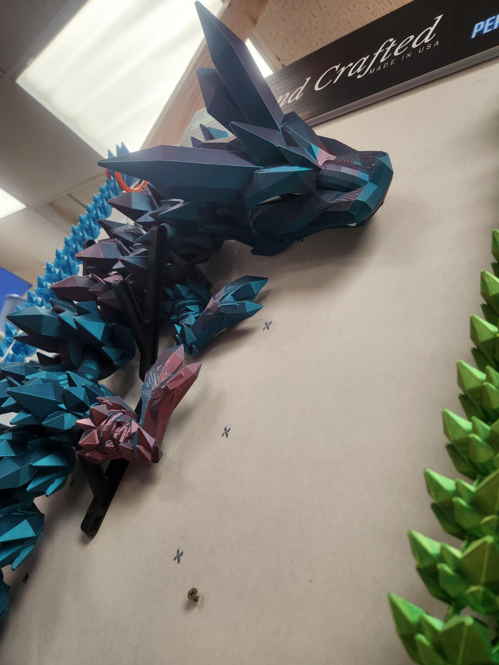 3D printed polygonal dragon wall art with blue and green geometric spikes, displayed indoors.