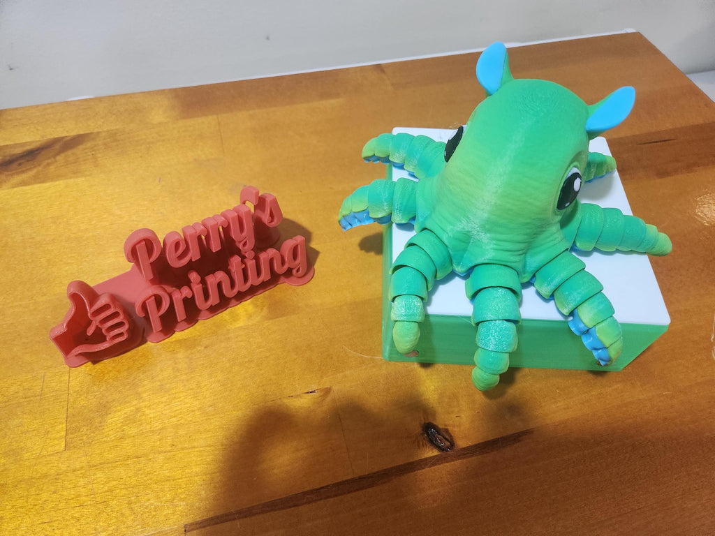 3D printed green articulated octopus and red Perry's Printing sign on wooden table