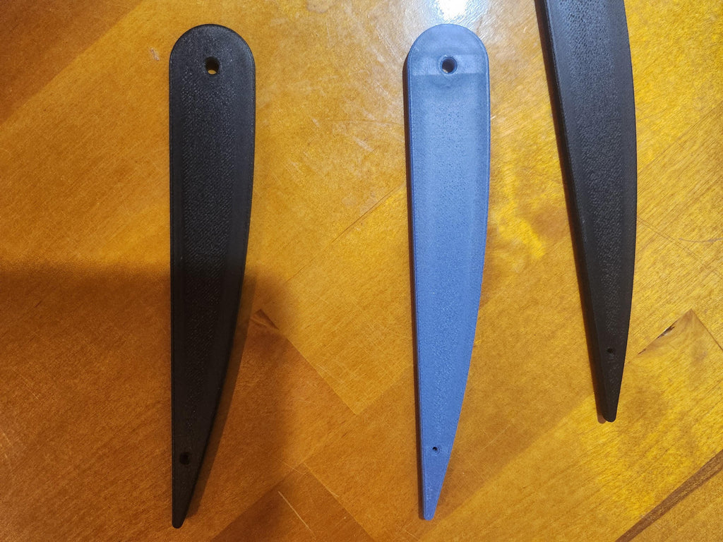Three 3D printed propeller blades, black and blue, displayed on a wooden surface.