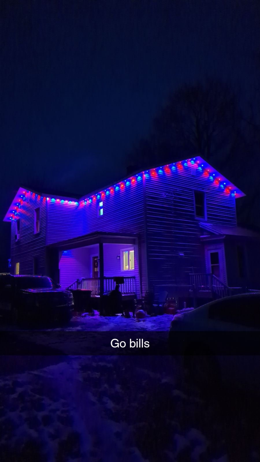 House at night with blue and red LED lights on roof, snow on ground, festive outdoor lighting