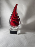 Red and clear glass teardrop award with black swirl design on a clear display base