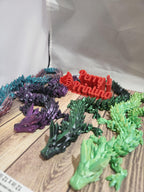 Colorful 3D printed articulated dragon figures on wood surface with Perry's Printing sign