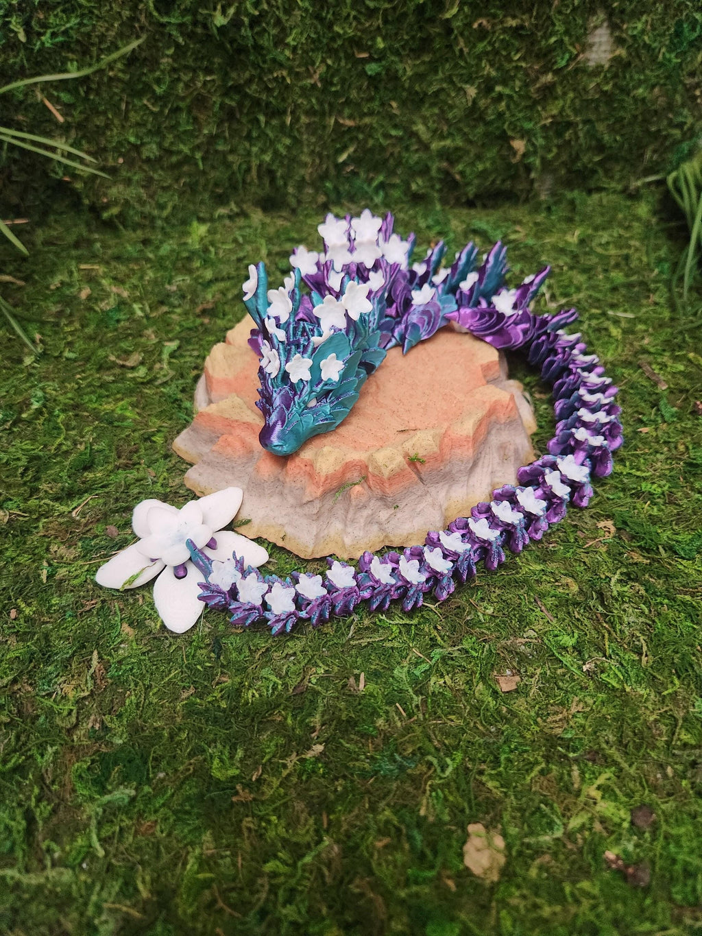 3D printed dragon with blue, purple, and white floral design on a mossy surface