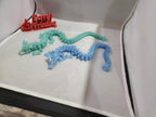 3D printed articulated dragon figures in blue and green on a display platform.