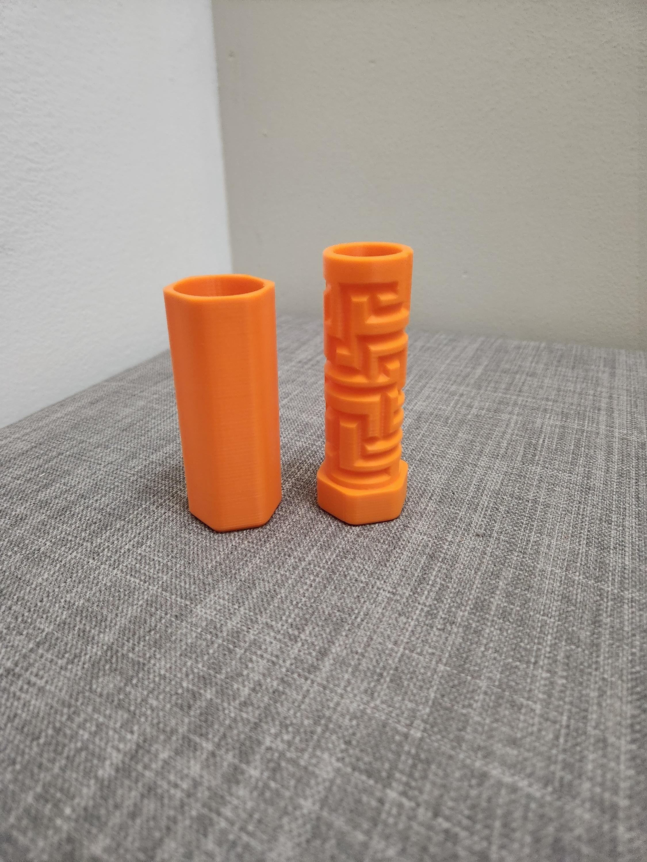 Two orange 3D printed cylindrical objects, one with a maze pattern, on a gray surface
