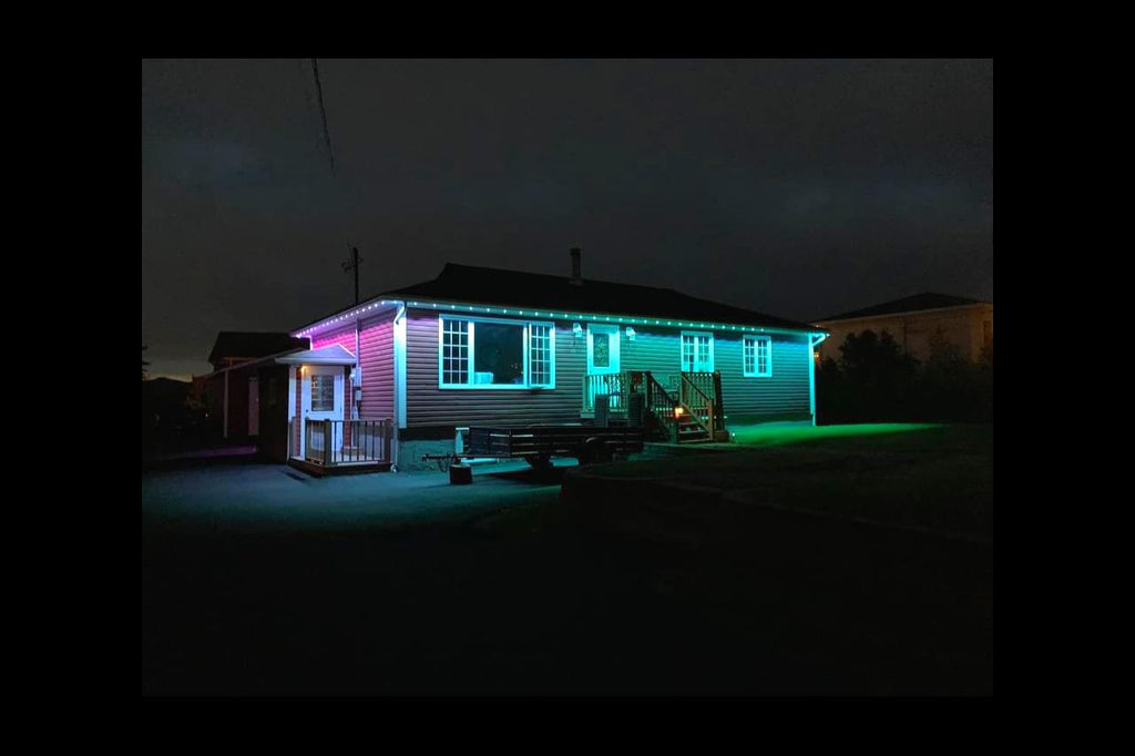 Single-story house at night with color-changing LED strip lights outlining the roof.