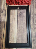 3D printed black plastic sign holder frame with mounting hole on wood surface