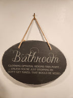 Funny engraved bathroom sign with humorous text, hanging on a wall with a rope.