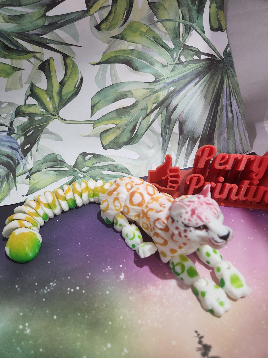 3D printed articulated leopard figure with colorful spots on a vibrant background, custom signage nearby