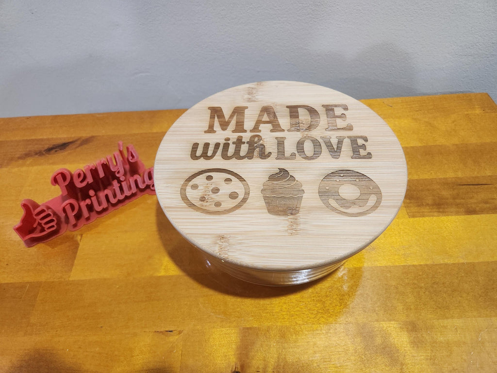 Laser engraved bamboo lid with 'Made with Love' and dessert icons on wooden table, 3D printed sign nearby.